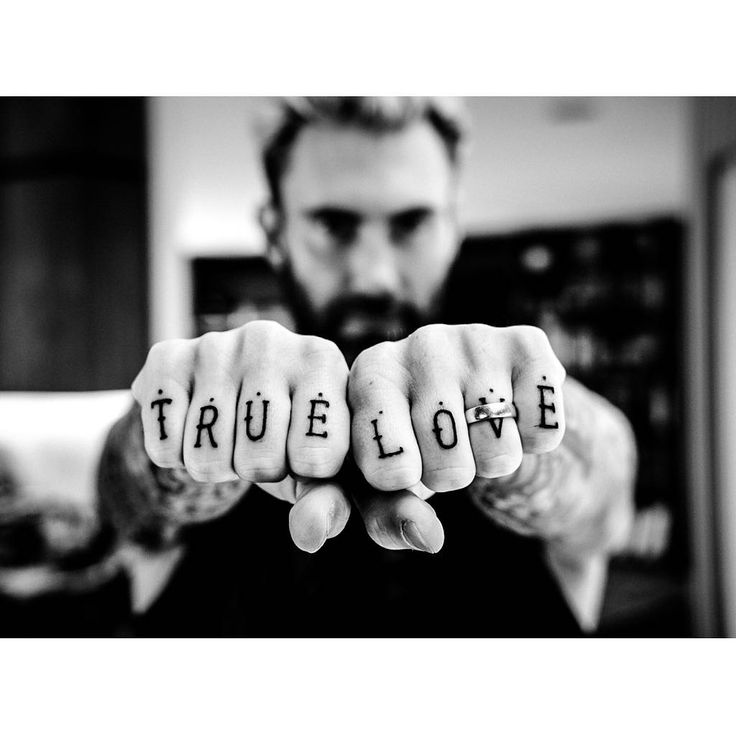 Adam Levine's hands held forward to show the True Love lettering across his knuckles