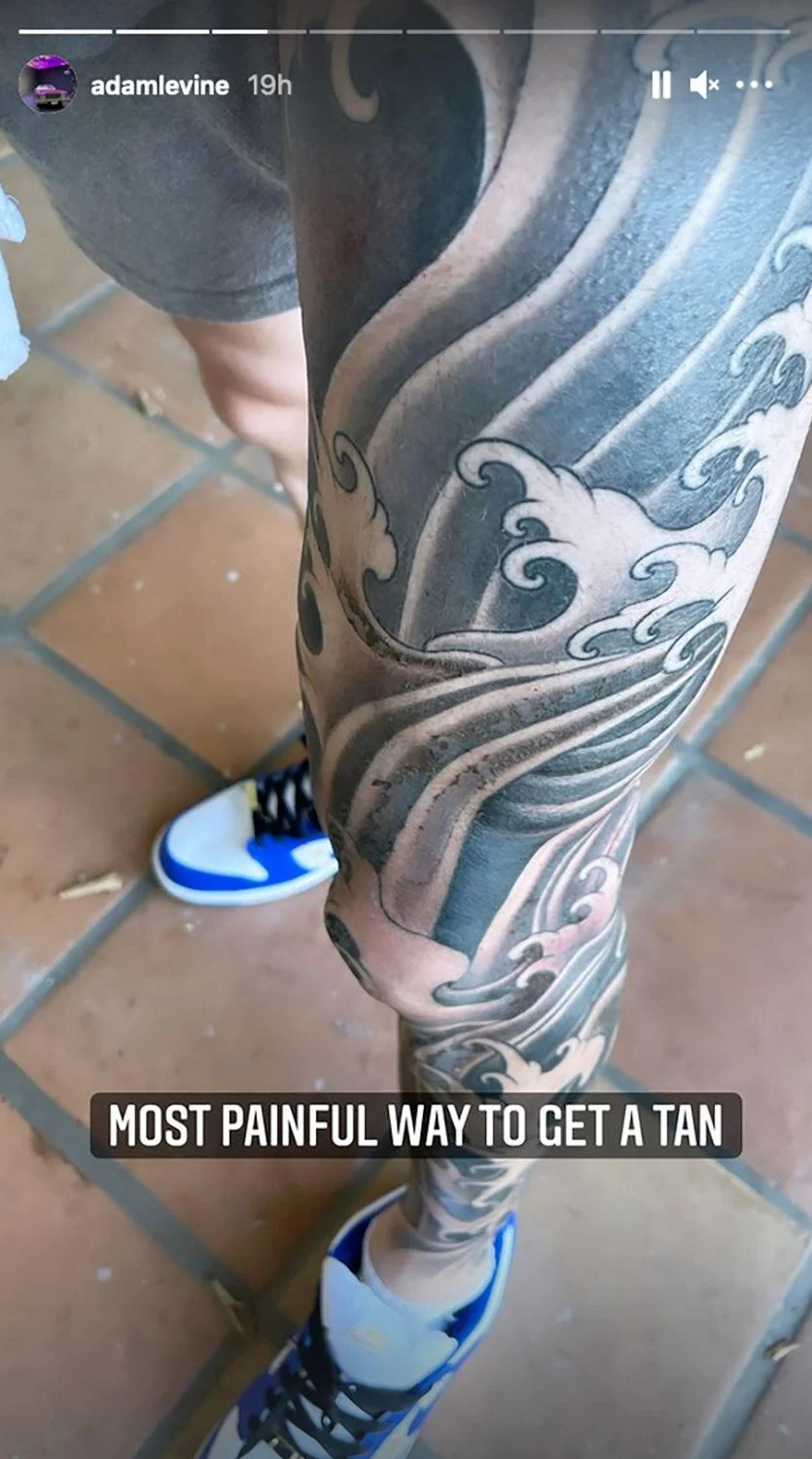 Adam Levine's large black-and-gray ocean wave tattoo wrapping from ankle toward the thigh on his left leg