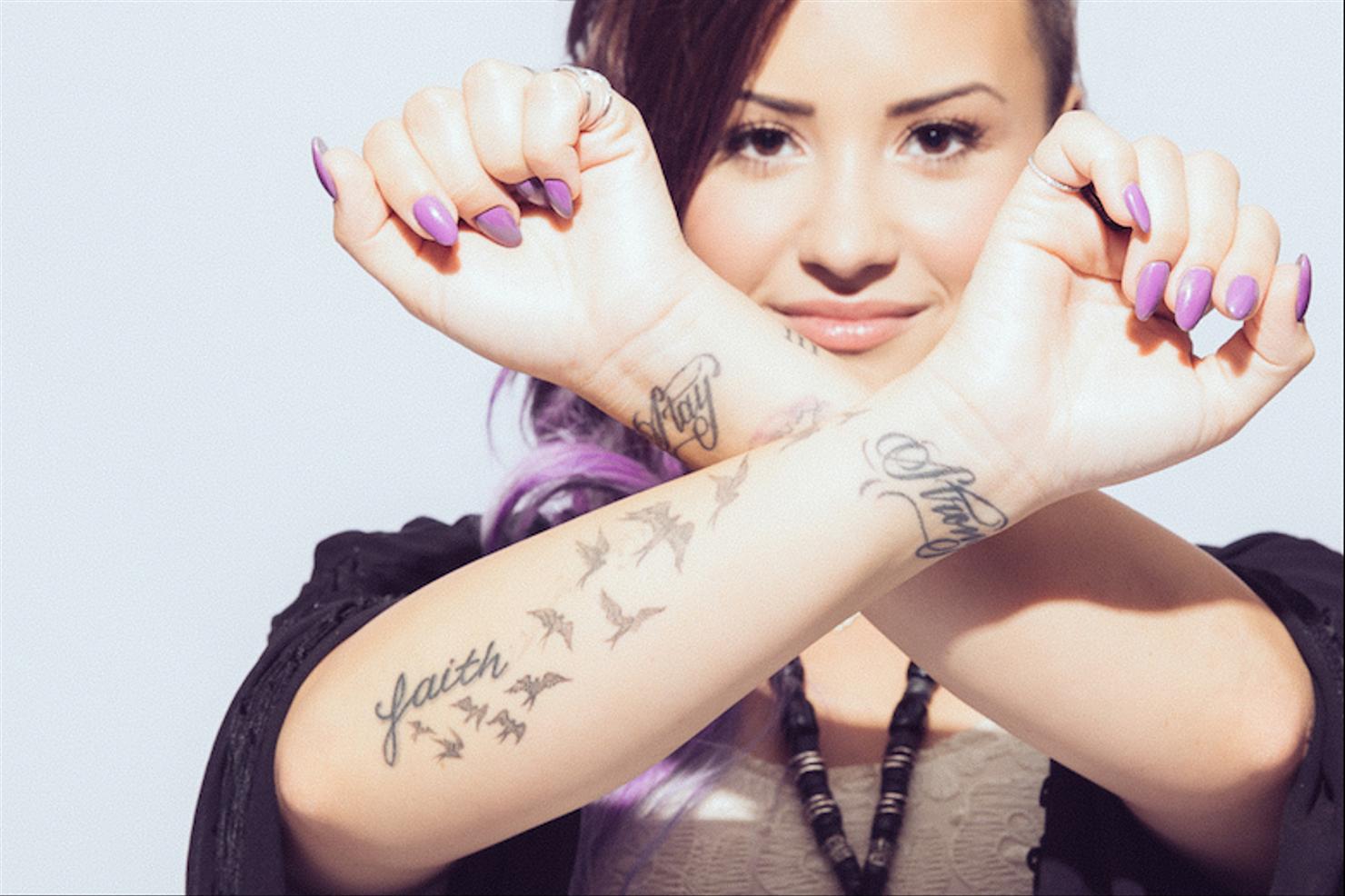 Demi Lovato shows the Stay Strong wrist lettering with her crossed forearms