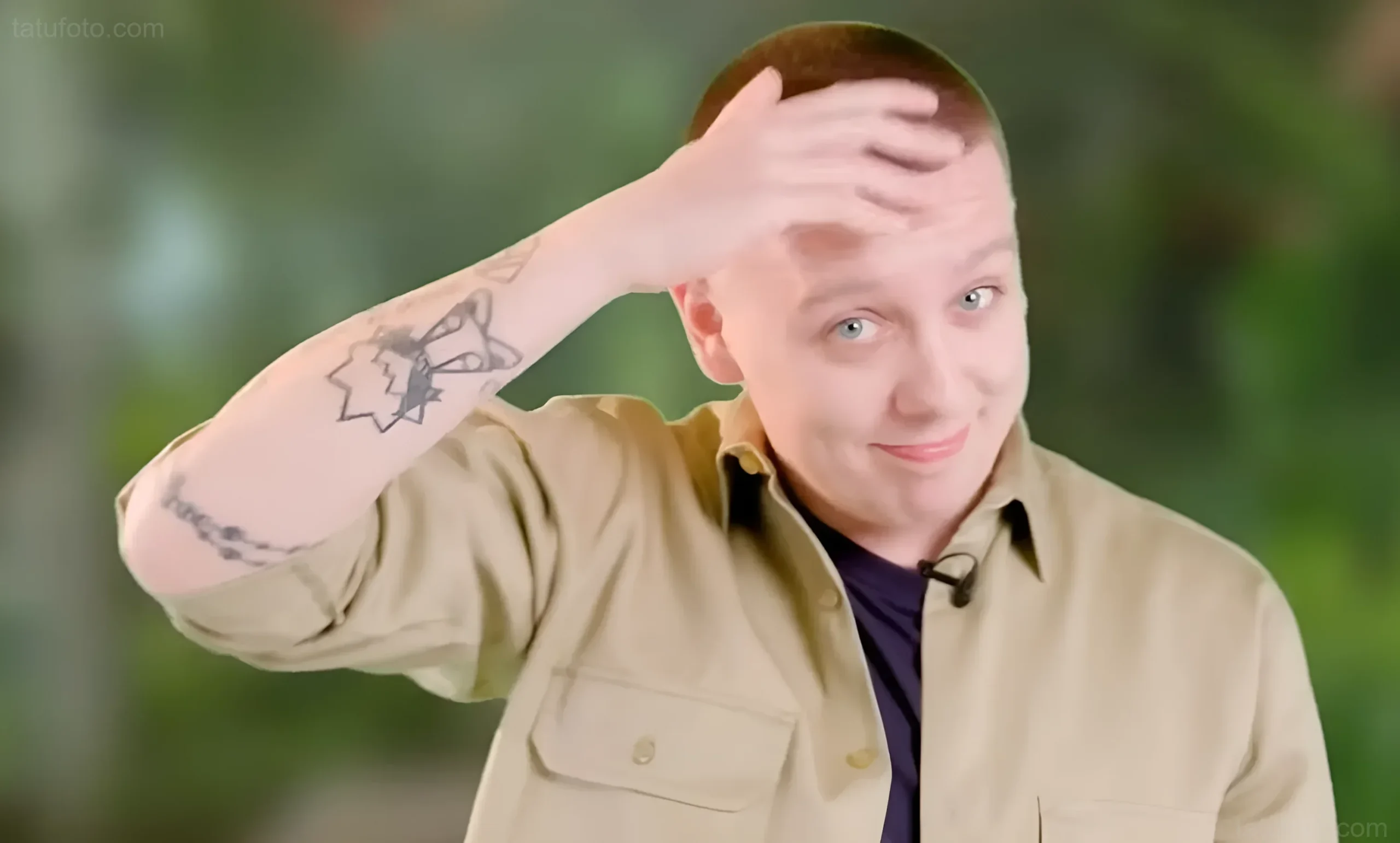 Aitch showing his rosary, arm and Manchester tattoos in a tattoo feature