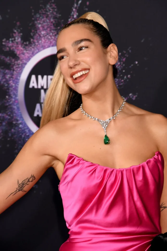 Dua Lipa showing the rose outline tattoo on her bicep