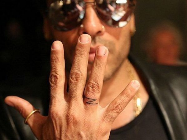 Lenny Kravitz raising his right hand to show the small Z tattoo on his ring finger