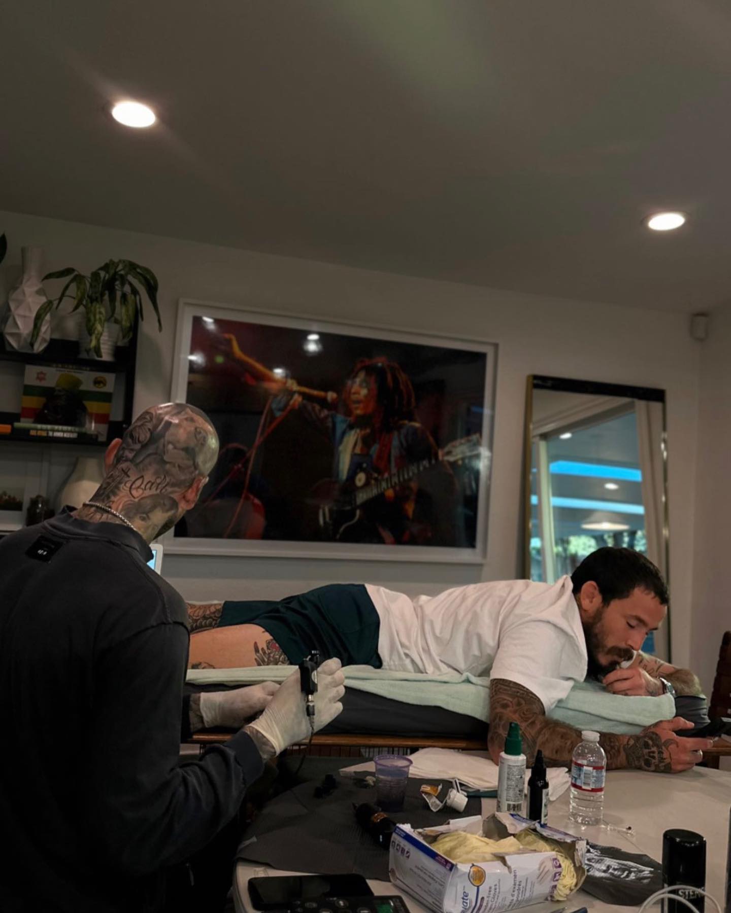 Marlon Vera during a tattoo session showing leg and lower-body ink