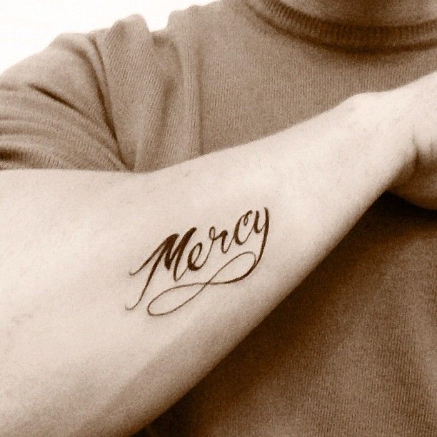 Close-up of Nick Jonas’s cursive Mercy tattoo with an infinity-shaped flourish on his forearm