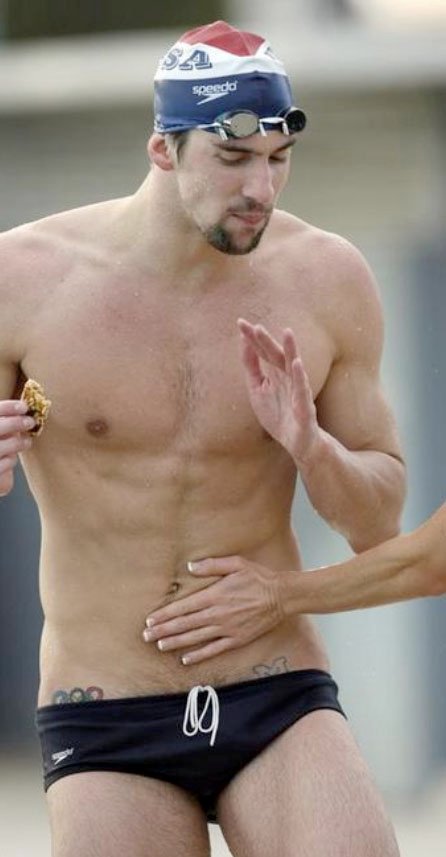 Michael Phelps showing small tattoos on both hips beside a pool
