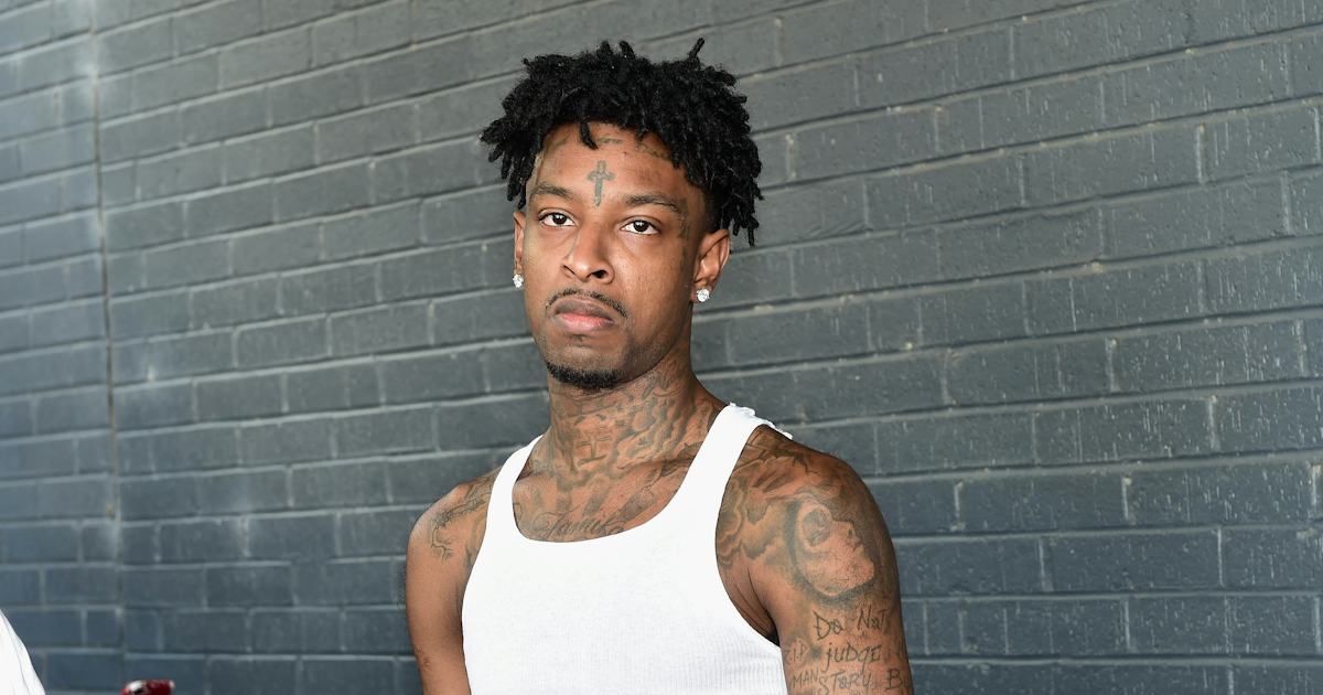 21 Savage in a white tank top showing chest and face tattoos