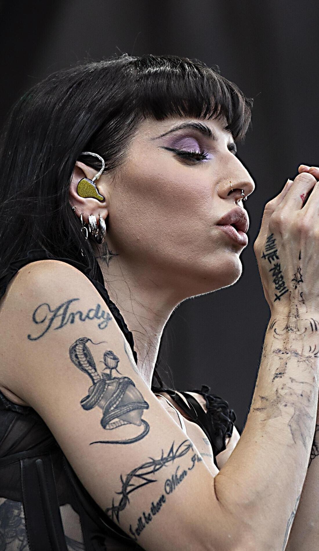 Lilith Czar tattoos: close stage portrait showing the Andy lettering, snake-like arm work and other visible ink while she performs