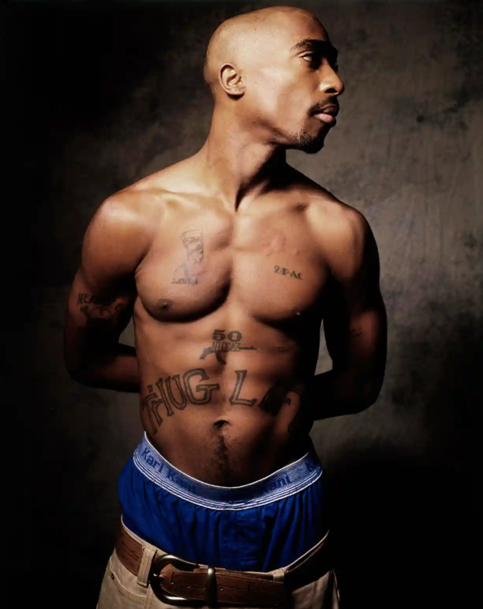 Tupac Shakur tattoos: large, clean front portrait showing the Thug Life stomach lettering, 50 Niggaz mark and chest tattoos