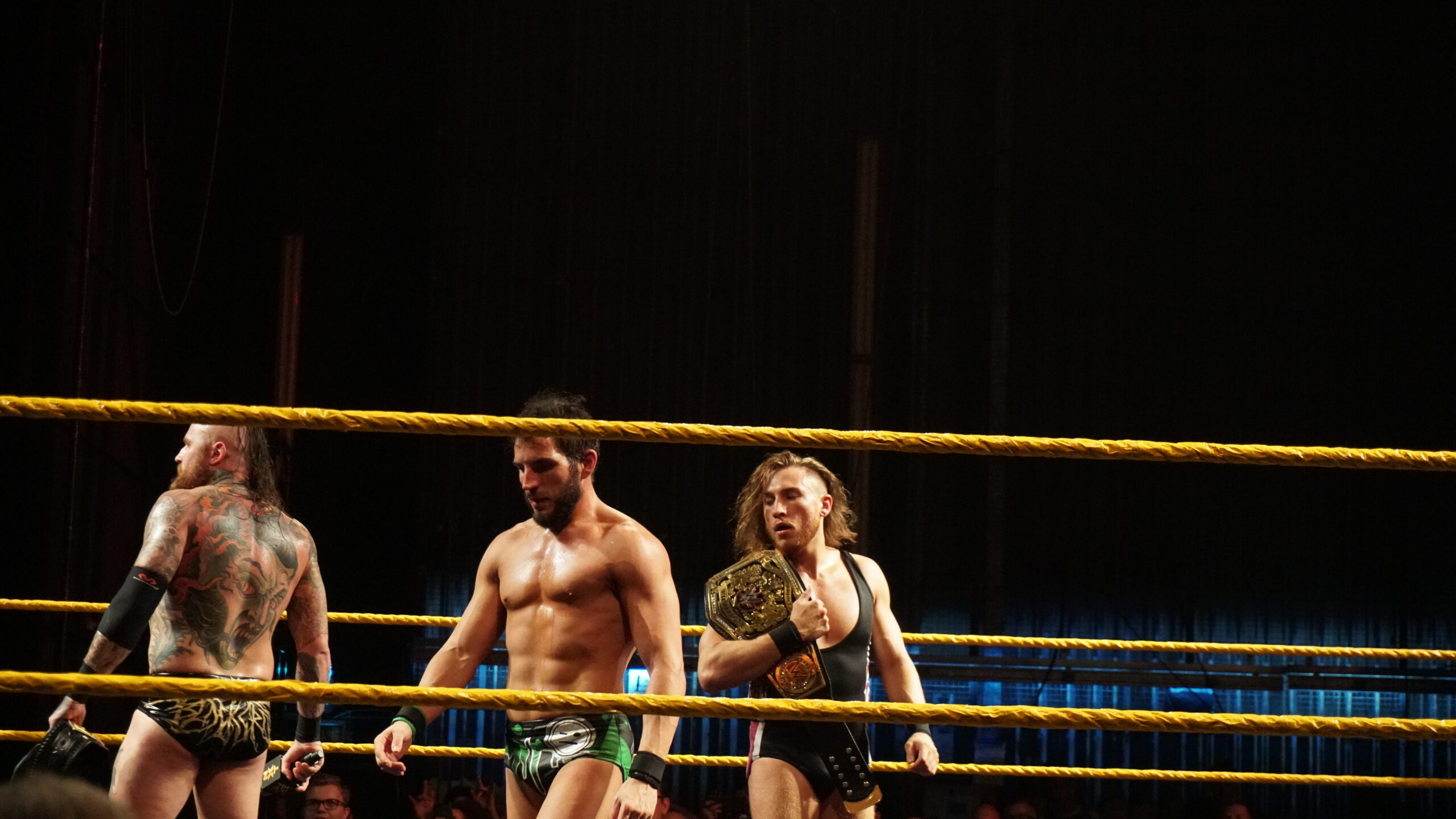 Malakai Black tattoos: high-resolution wrestling photograph showing Malakai Black's large back tattoo and upper-arm coverage from behind