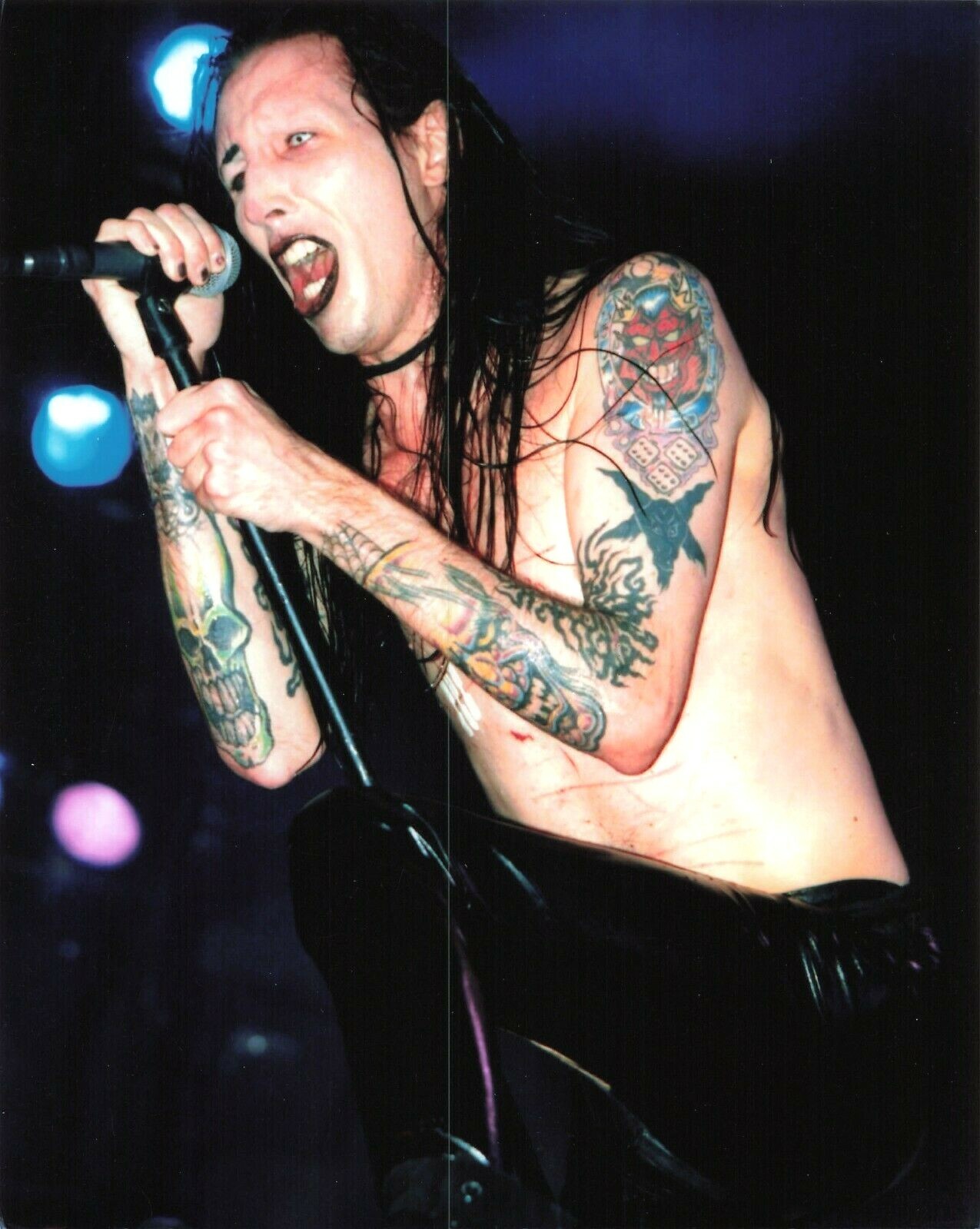 Marilyn Manson tattoos: large shirtless stage photograph where skull, dice and dark arm tattoos are visible together