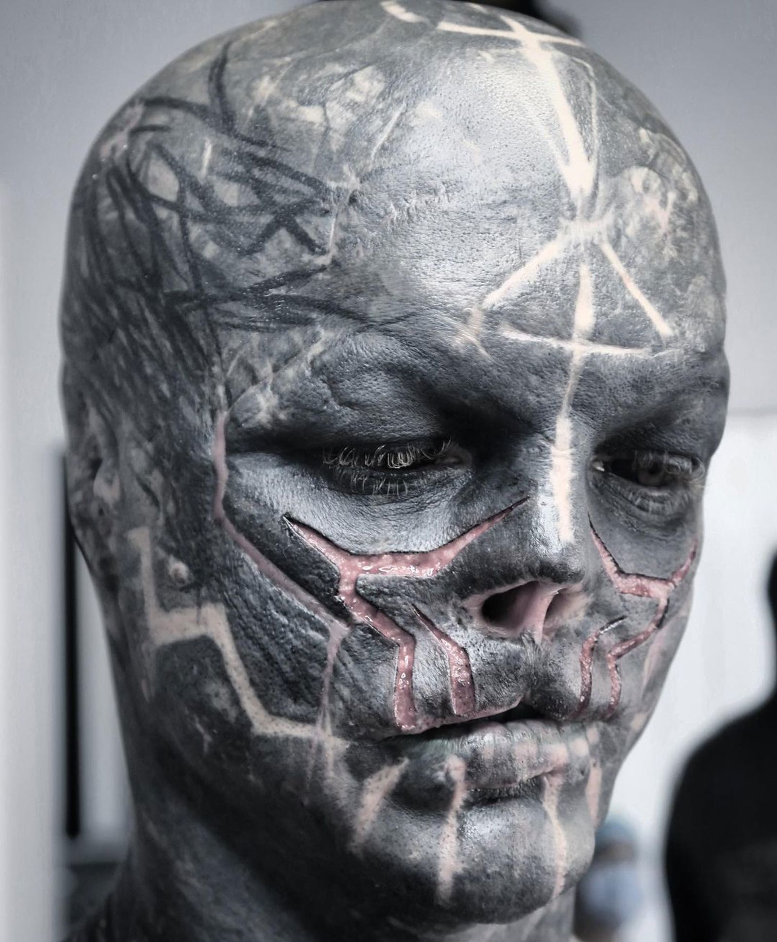 Anthony Loffredo tattoos: sharp close-up showing the black face tattoos, pale geometric lines, scar-like texture and head implants