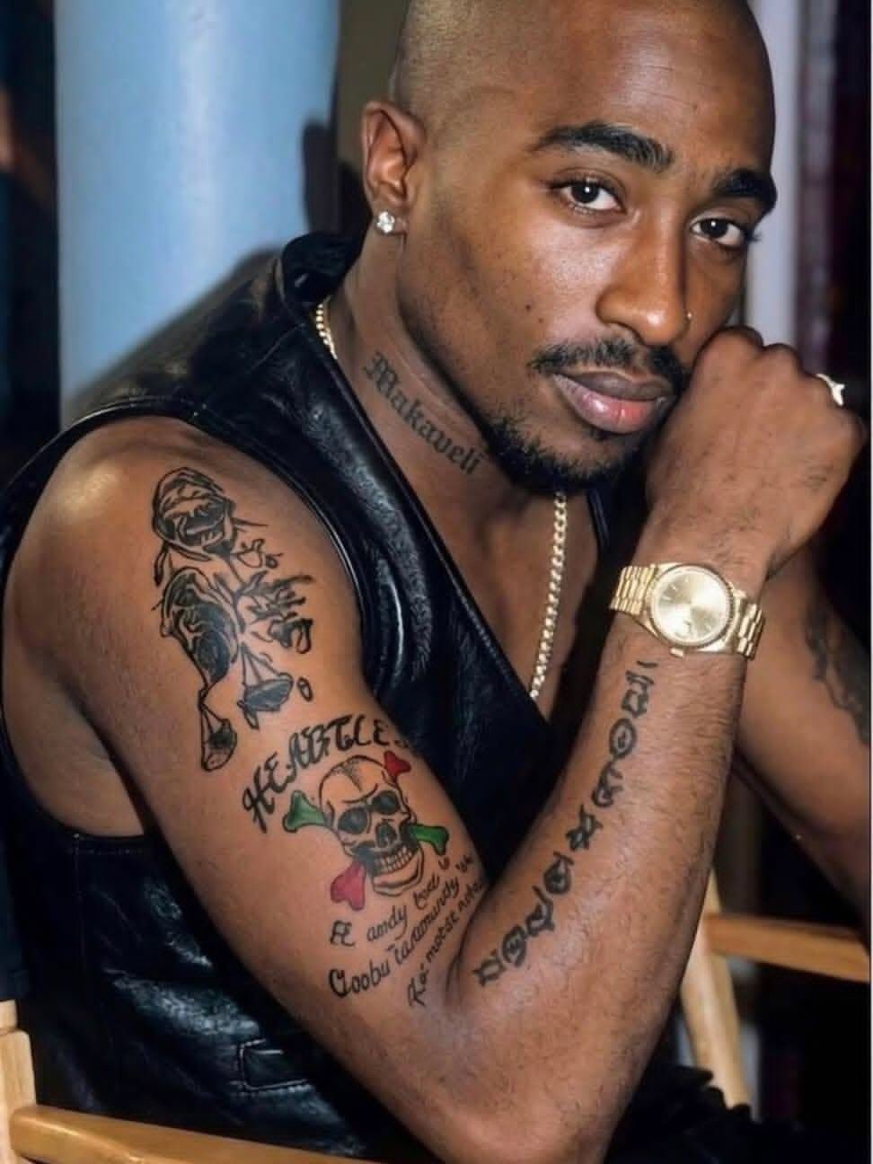 Tupac Shakur tattoos: sharp face-visible photograph showing the Makaveli neck tattoo, Heartless skull and script on the arm