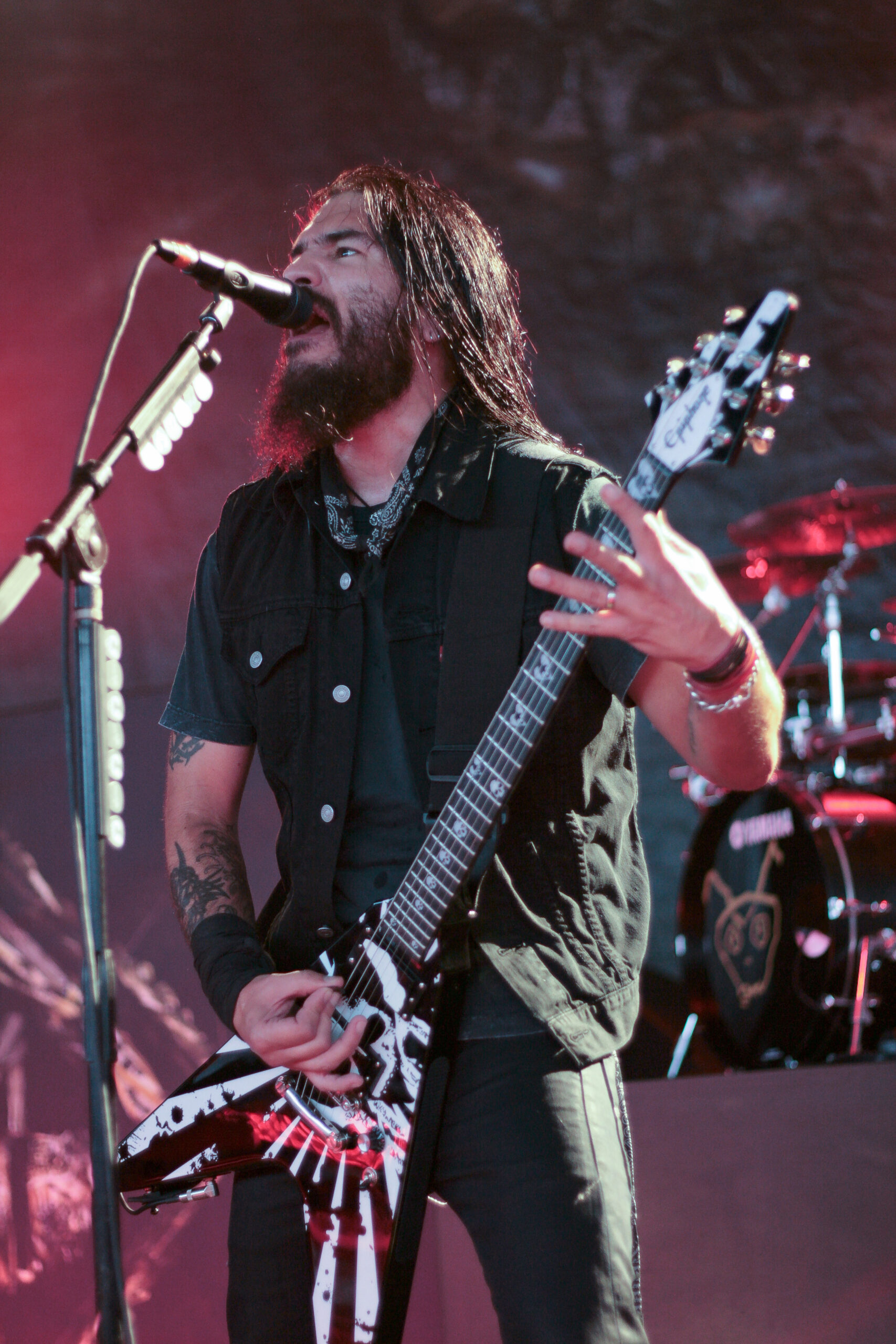Robb Flynn tattoos: large vertical concert photograph showing the upper-arm emblem, forearm coverage and tattoo placement around the guitar strap