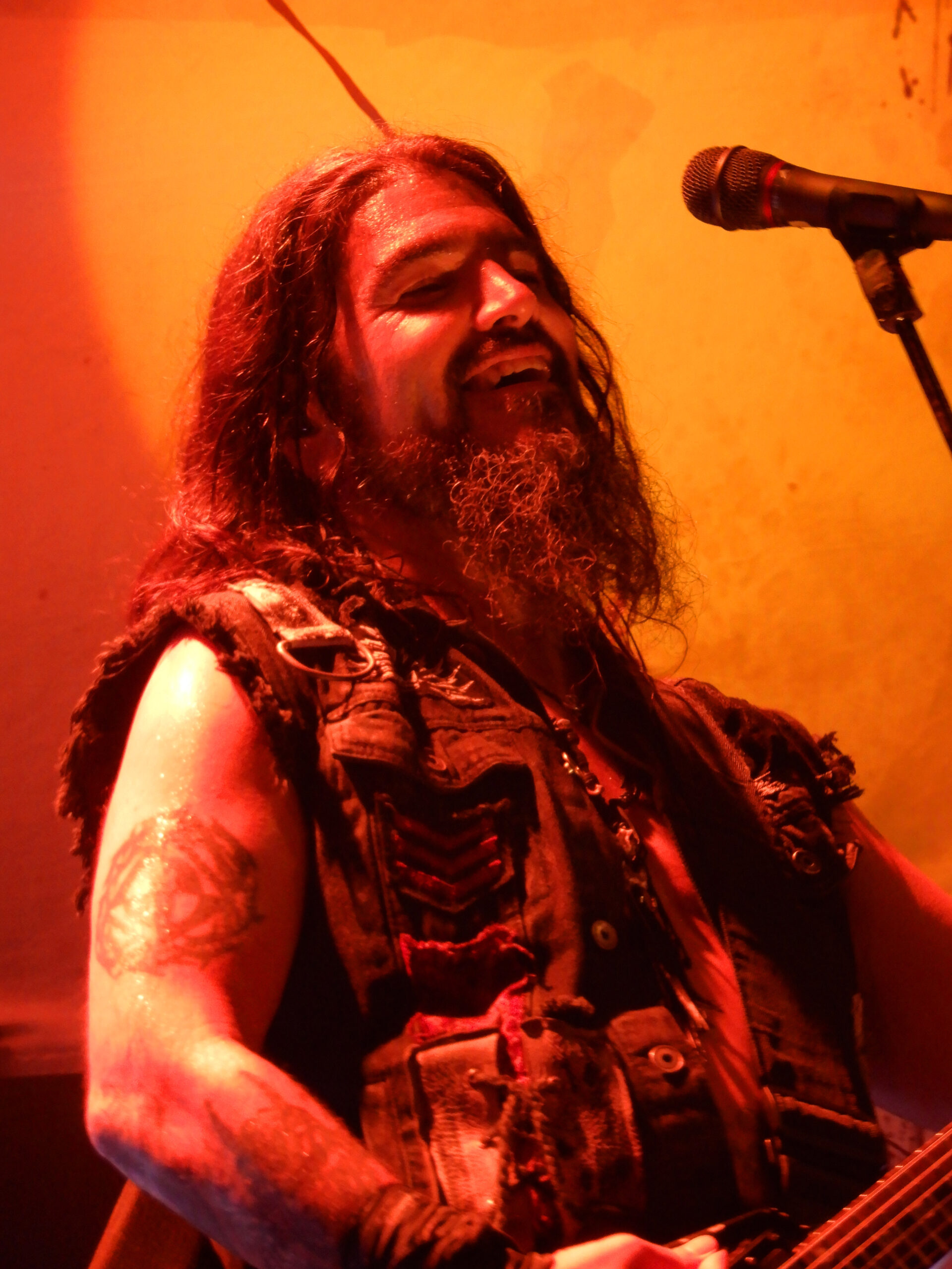 Robb Flynn tattoos: high-resolution live photograph showing the separate upper-arm emblem and the dense lower-arm tattoo work