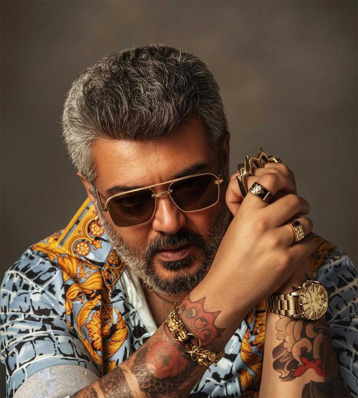 Ajith Kumar tattoos: separate close portrait exposing Ajith Kumar's forearm tattoos in a patterned shirt