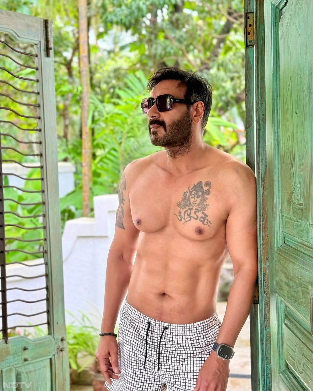 Ajith Kumar tattoos: separate shirtless doorway photograph where the chest design and face are both visible