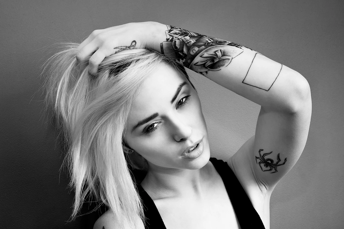 Alysha Nett spider, upper-arm and forearm tattoos Alysha Nett tattoos: black-and-white face-visible portrait showing the upper-arm piece, mechanical forearm detail and small spider tattoo