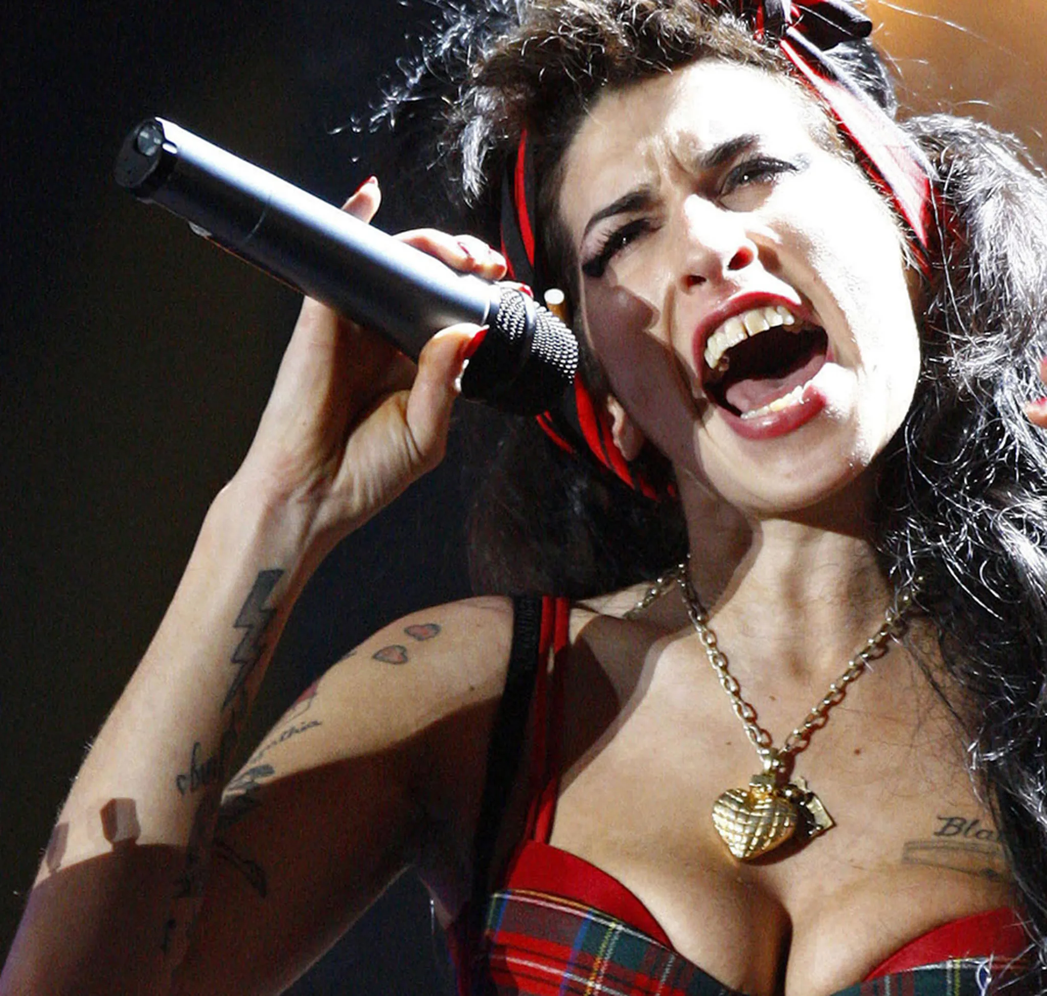 Amy Winehouse live performance with visible arm, chest, and shoulder tattoos