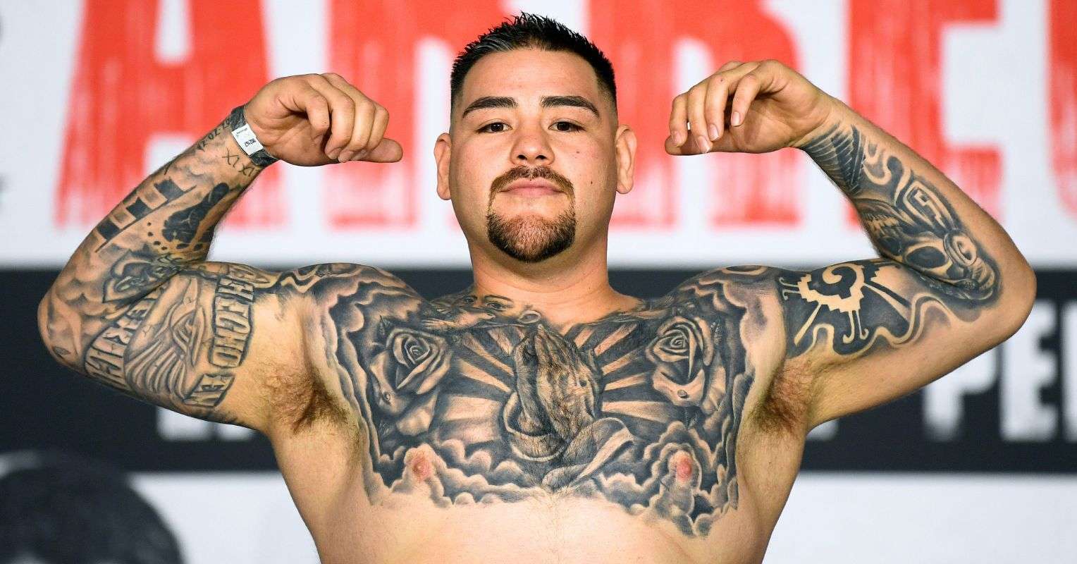 Andy Ruiz Jr. tattoos: shirtless press portrait with the tattooed chest, roses, central religious imagery, and both arms visible