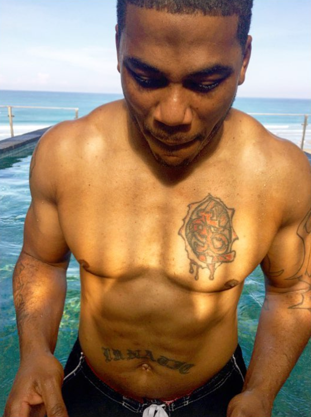 Nelly tattoos: sunlit close portrait showing the chest emblem and lower stomach script without stage clothing