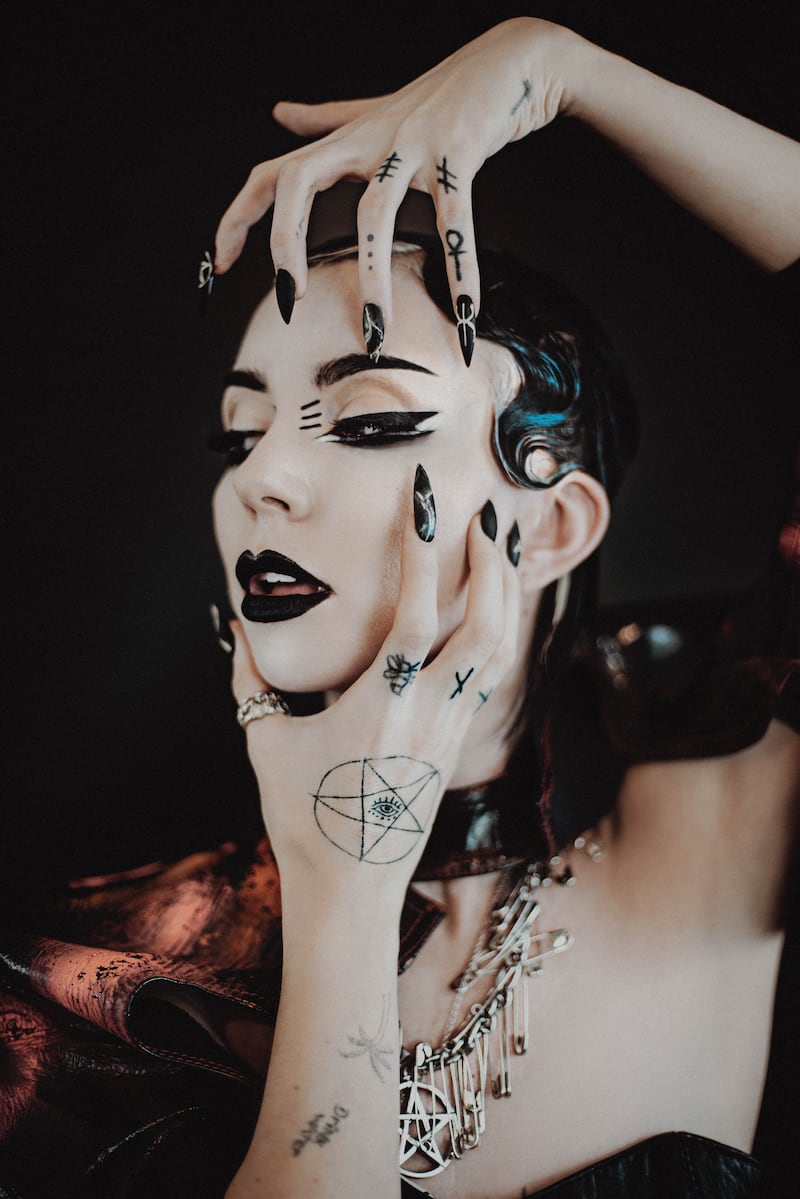 Bambie Thug tattoos: close face-visible portrait showing finger symbols, hand ink and a pentagram eye tattoo