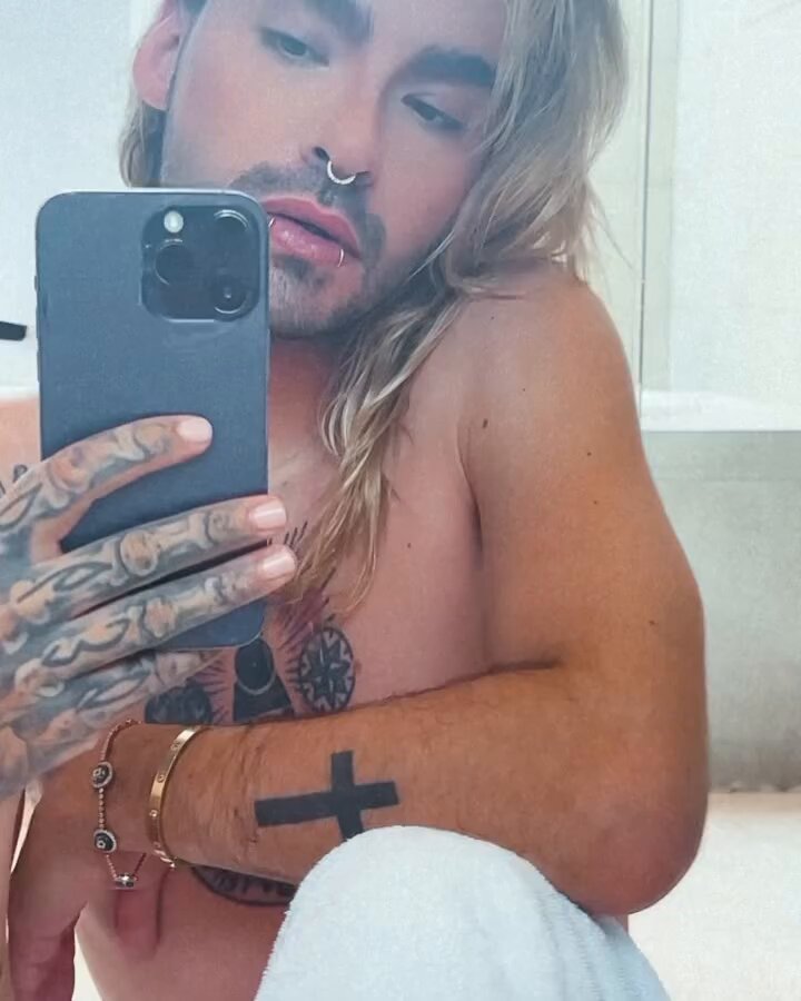 Bill Kaulitz tattoos: high-resolution mirror selfie where the tattooed hand, solid forearm cross and central chest emblem are plainly visible