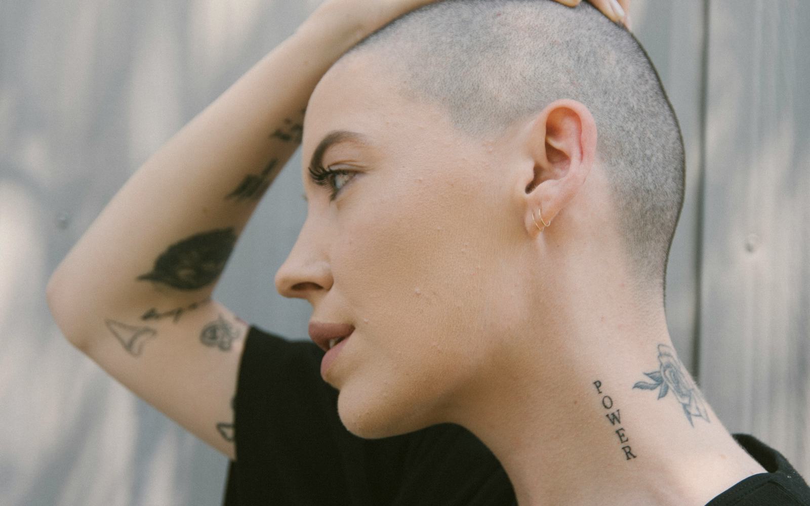 Bishop Briggs tattoos: Close editorial tattoo photograph showing POWER neck lettering, floral neck ink and forearm tattoos.
