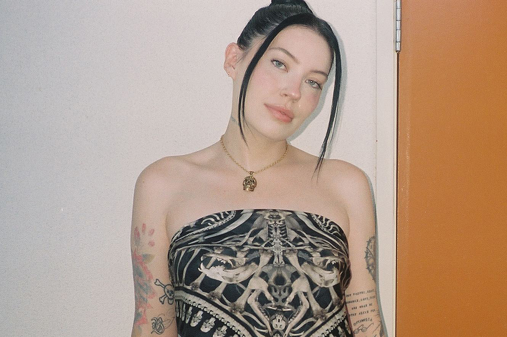 Bishop Briggs tattoos: Portrait clearly showing colourful and black illustrative tattoos across both arms.