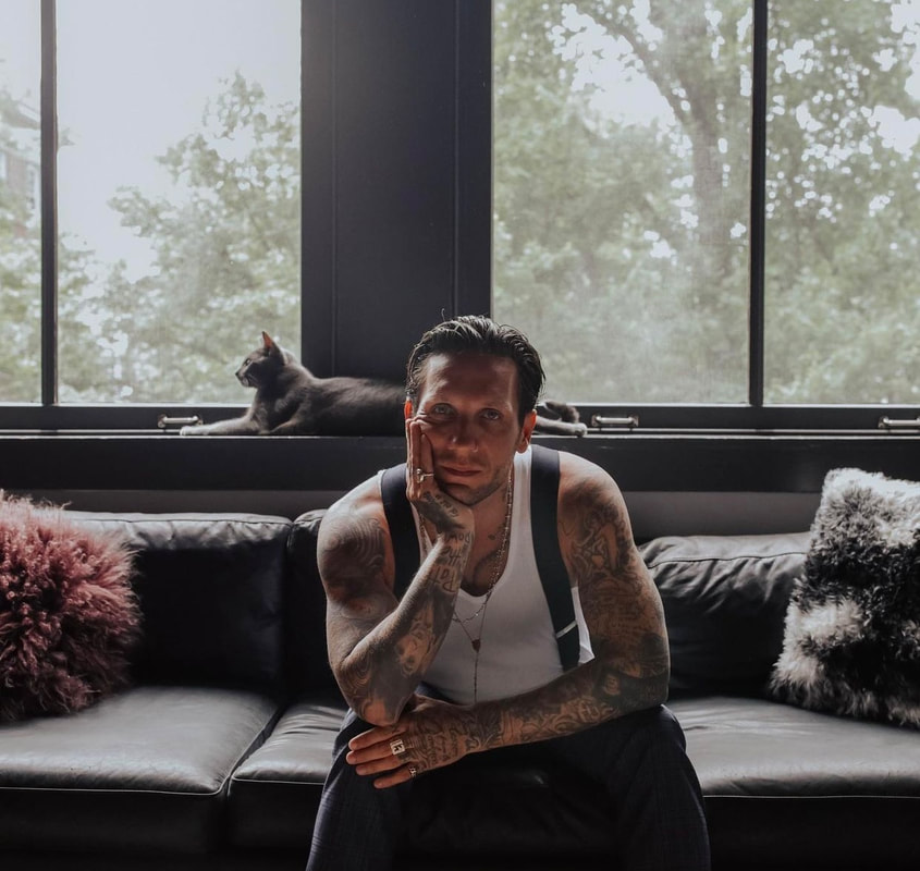 Brandon Novak tattoos: high-resolution seated portrait showing both dense sleeves, chest and hand tattoos