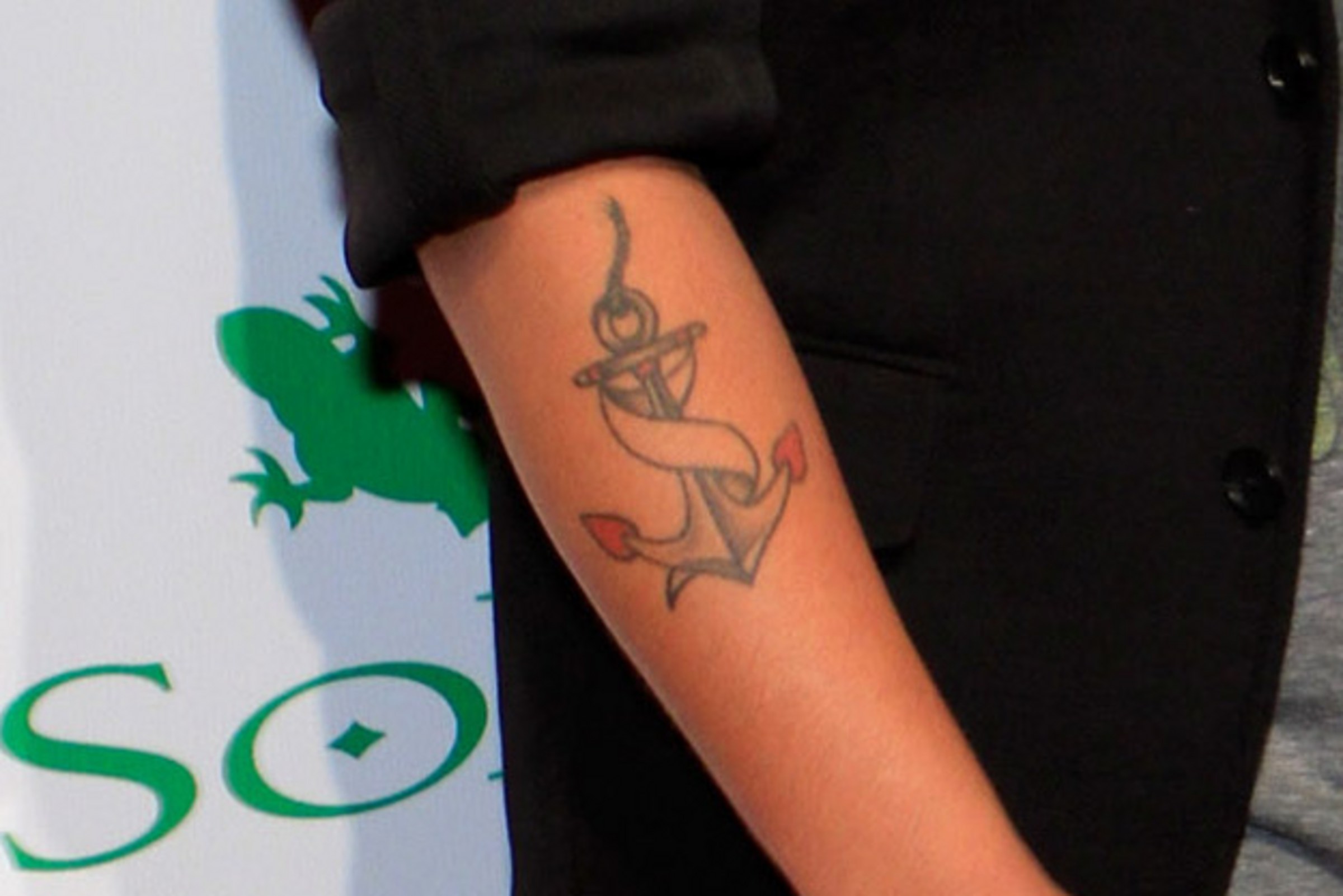 Bruno Mars tattoos: close-up of Bruno Mars’s gray rope-wrapped anchor with red fluke accents on the forearm