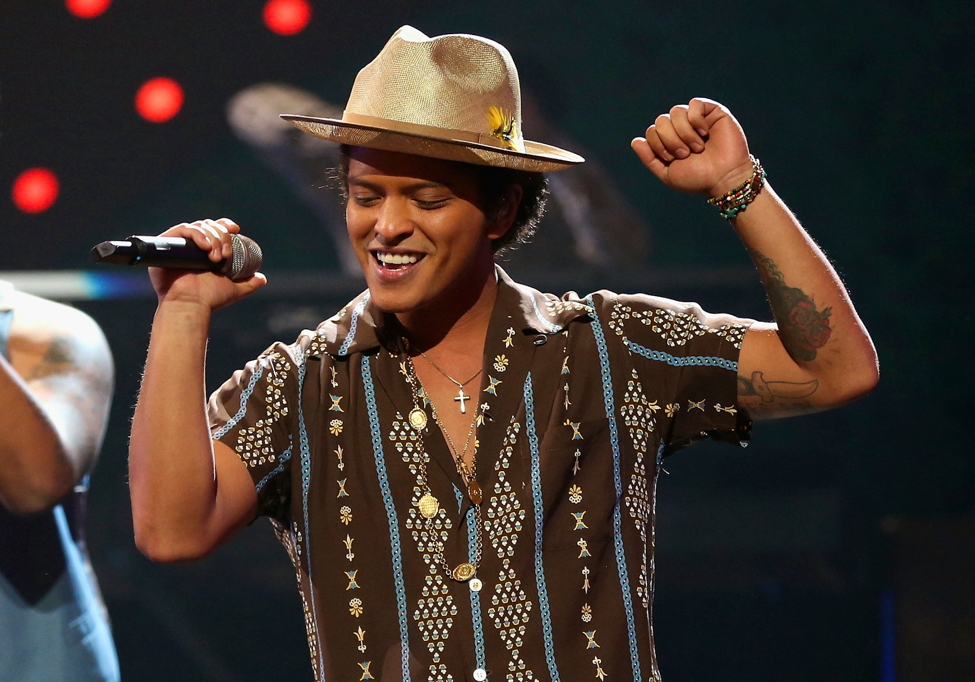 Bruno Mars tattoos: separate performance photograph showing the rose and linework across Bruno Mars’s raised arm