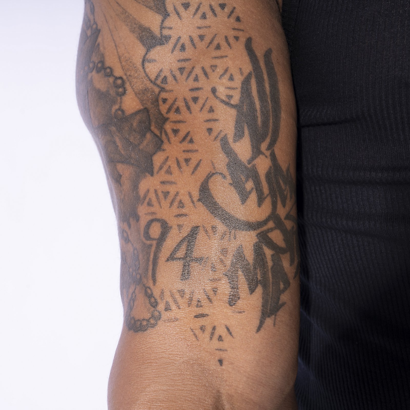 Carmelo Hayes tattoos: Upper arm lettering tattoo: All Eyes on Me