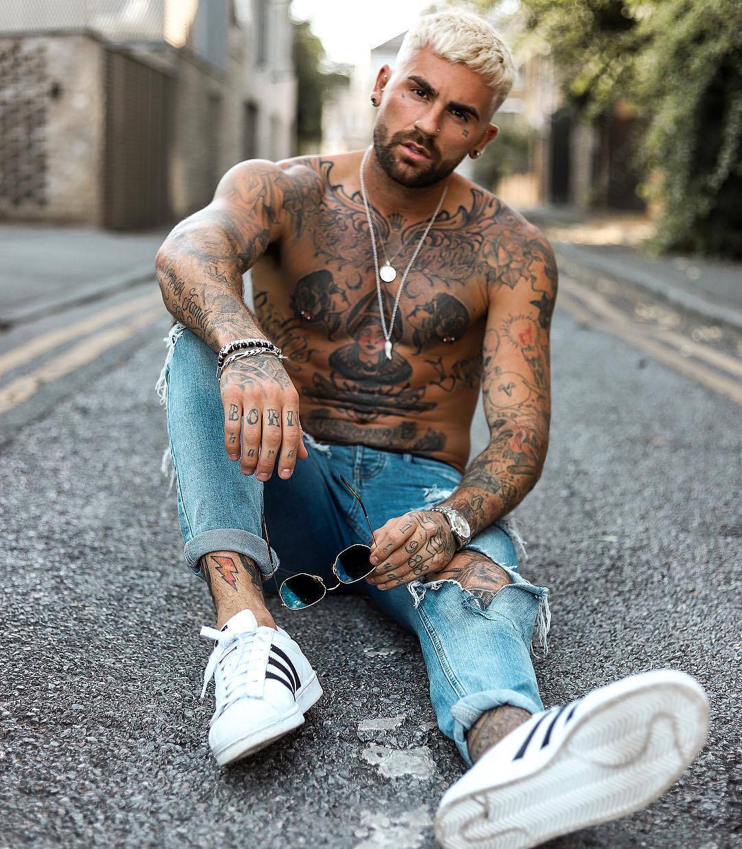 Chris Perceval tattoos: BORN finger lettering on Chris Perceval’s right hand resting over his knee