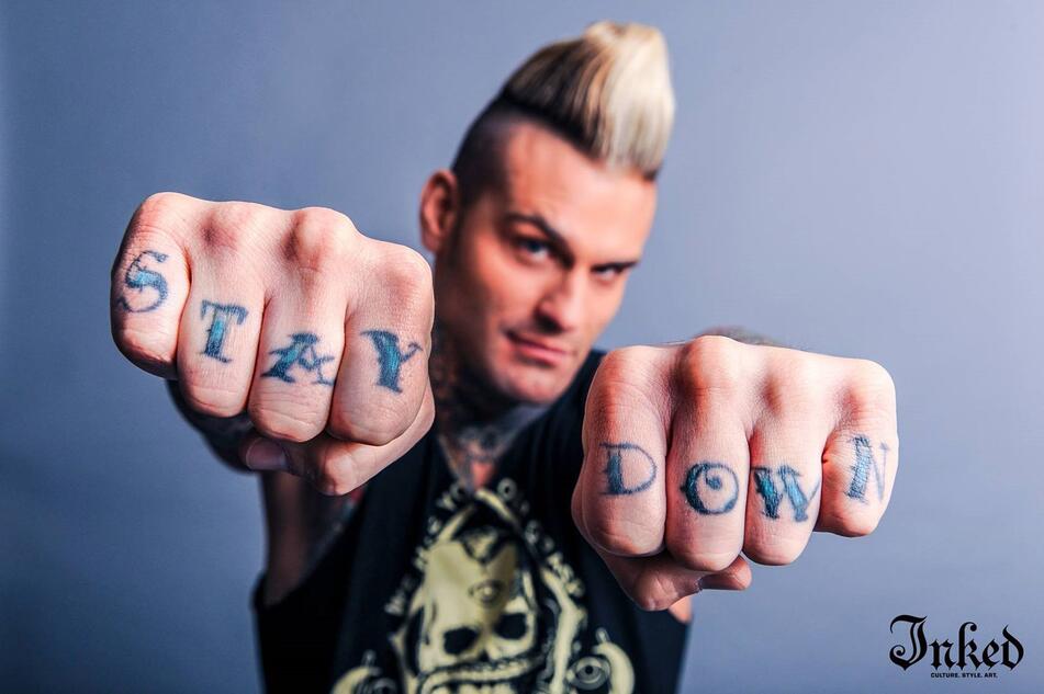 Corey Graves tattoos: STAY DOWN lettering visible across both knuckles in a distinct WWE/Inked editorial photograph