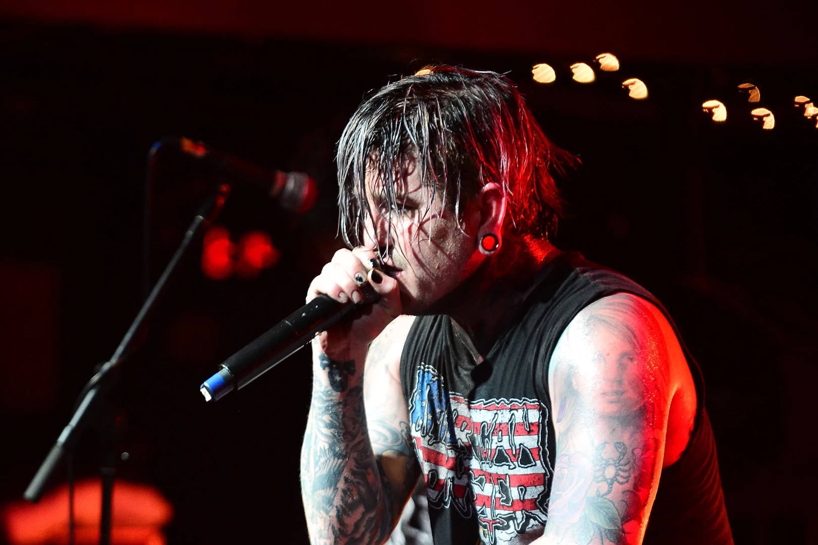 Craig Mabbitt tattoos: sharp red-lit close view showing layered forearm and upper-arm tattoo coverage