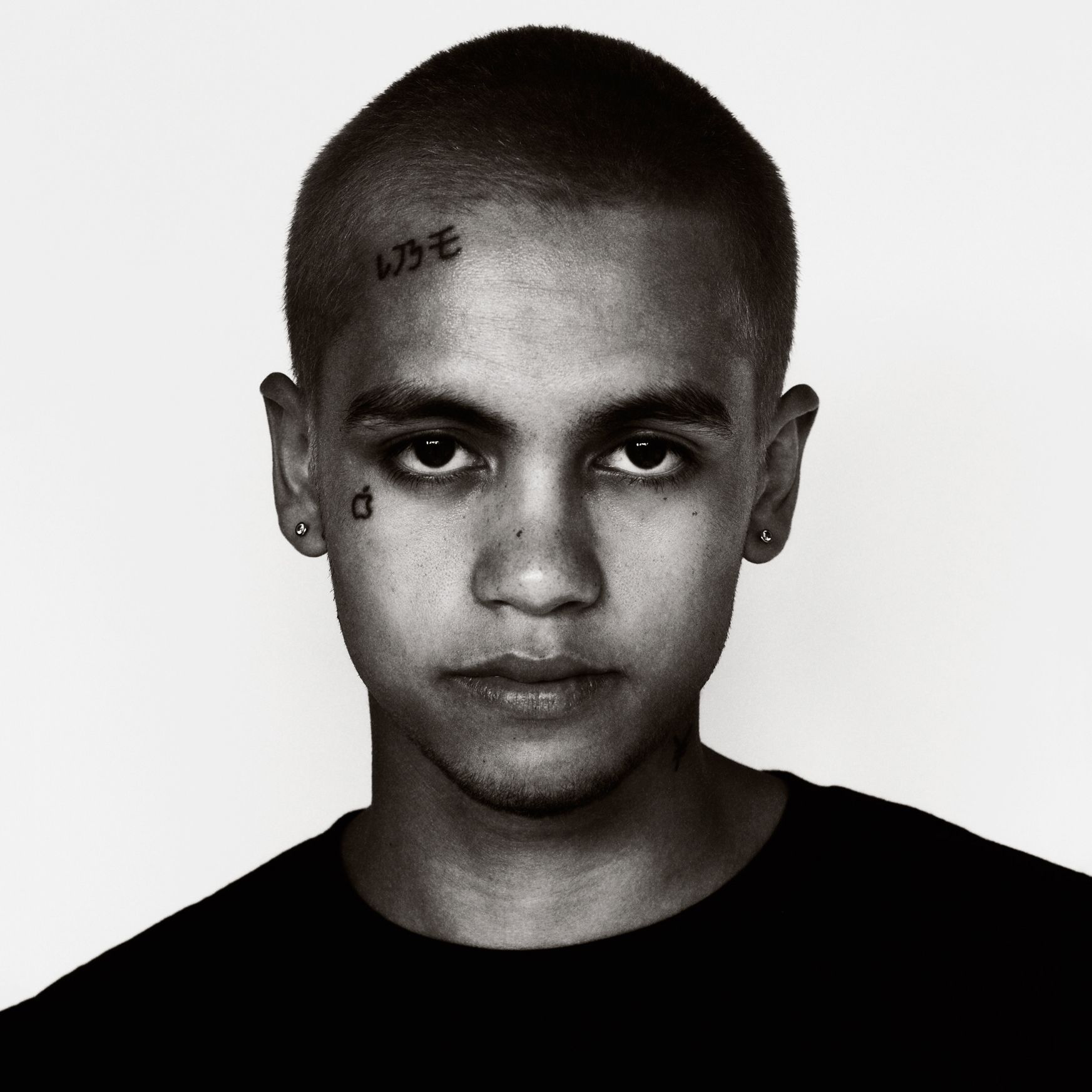 Dominic Fike tattoos: apple tattoo, forehead lettering, and small eye-area marks