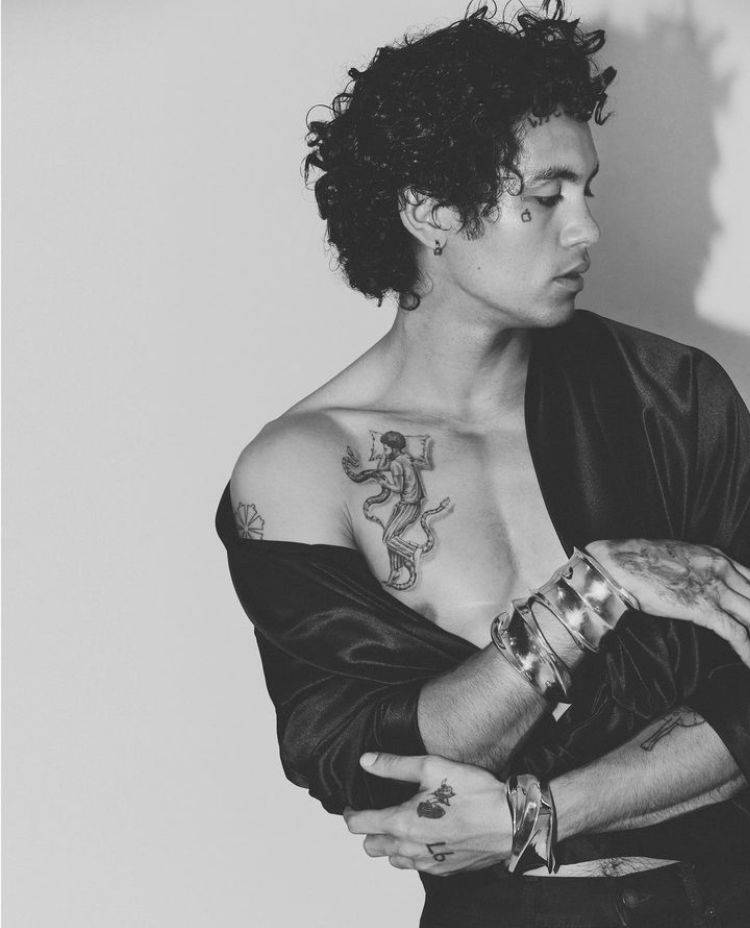 Dominic Fike tattoos: fine-line chest figure, shoulder outline, and visible hand ink