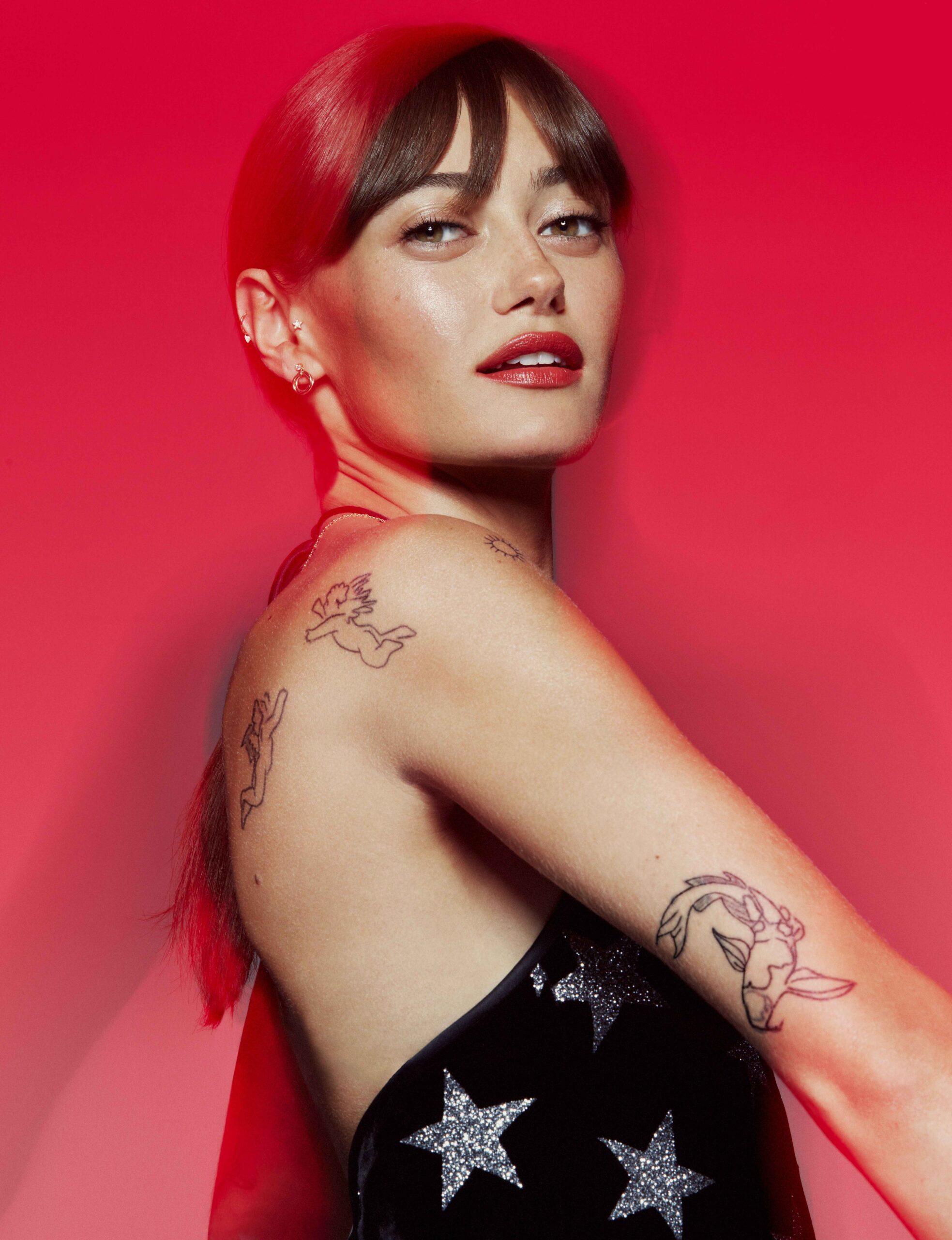 Ella Purnell tattoos: HUNGER portrait showing the cherub figures and larger outlined tattoo on the shoulder and upper arm