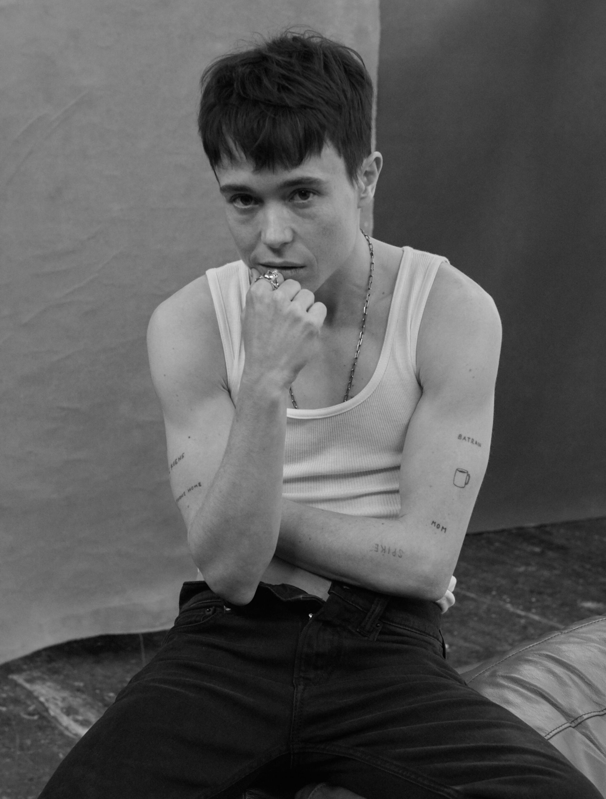 Elliot Page tattoos: Seated studio portrait with the small coffee cup visible on the arm