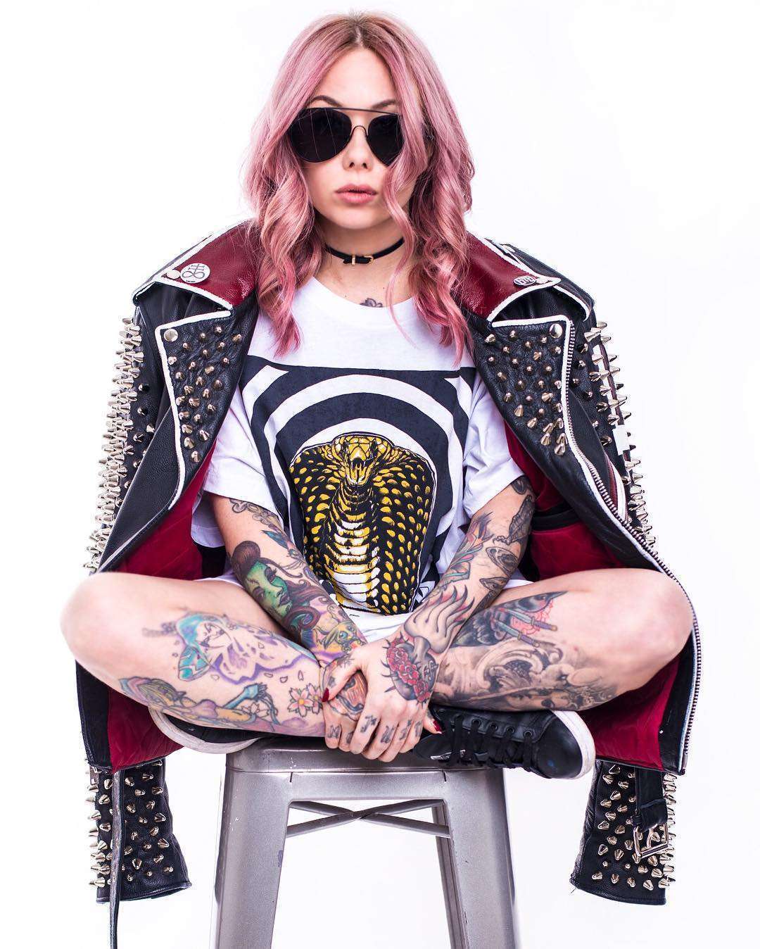 Hannah Snowdon tattoos: pink hair seated portrait showing arm and leg tattoos