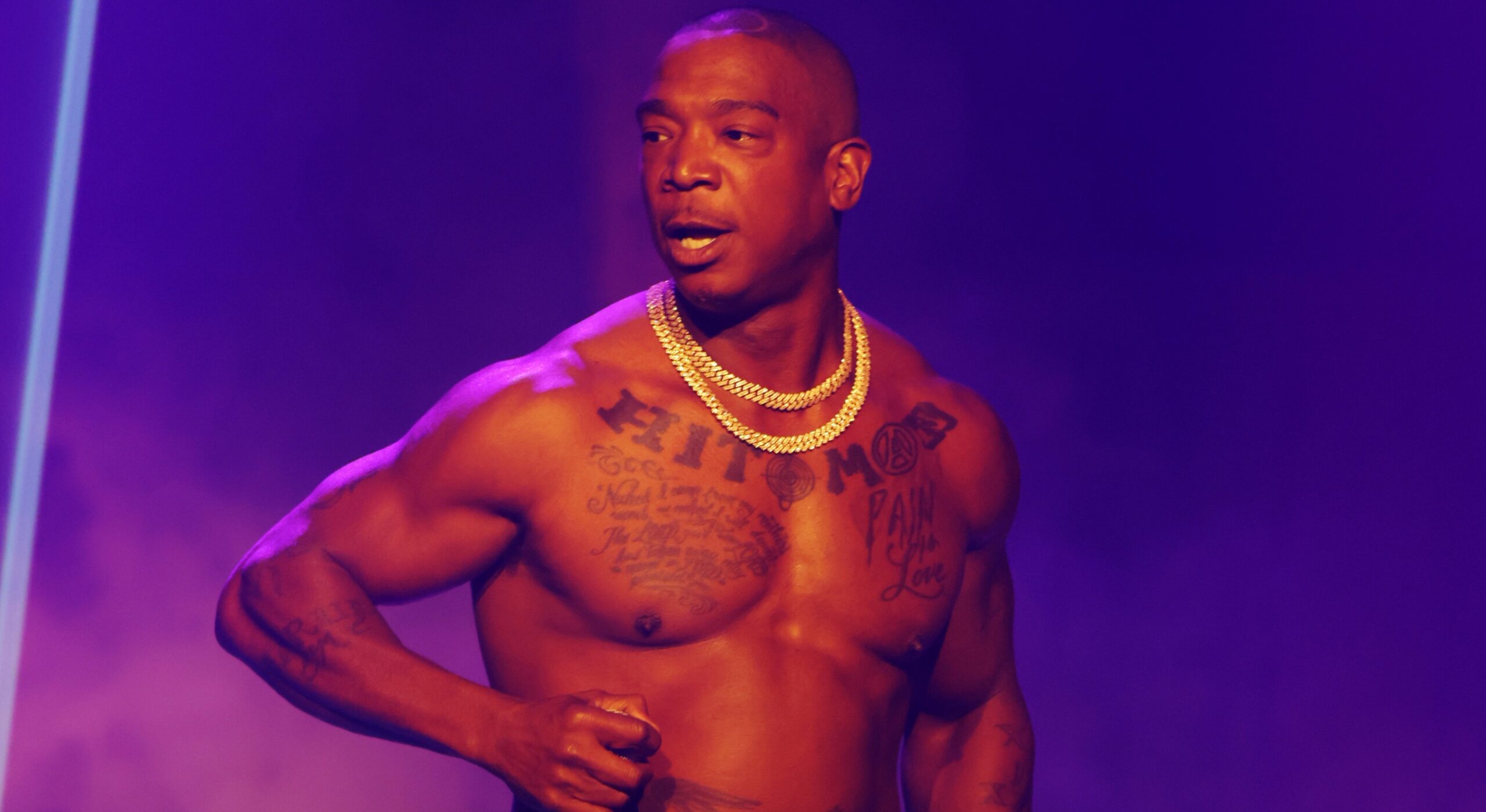 Ja Rule tattoos: high-resolution shirtless stage portrait clearly showing the Pain Is Love chest lettering and both arms