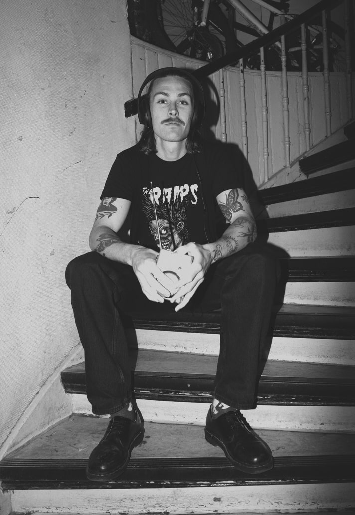 Jackson Irvine Distinct seated monochrome photograph with both tattooed arms visible; illustrates the range and patchwork arrangement of the arm work. Jackson Irvine tattoos: Distinct seated monochrome photograph with both tattooed arms visible; illustrates the range and patchwork arrangement of the arm work.