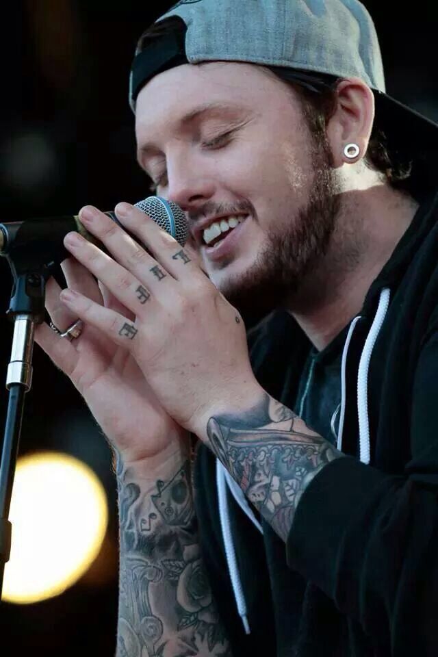 James Arthur tattoos: finger lettering and wrist tattoos visible during a live microphone performance