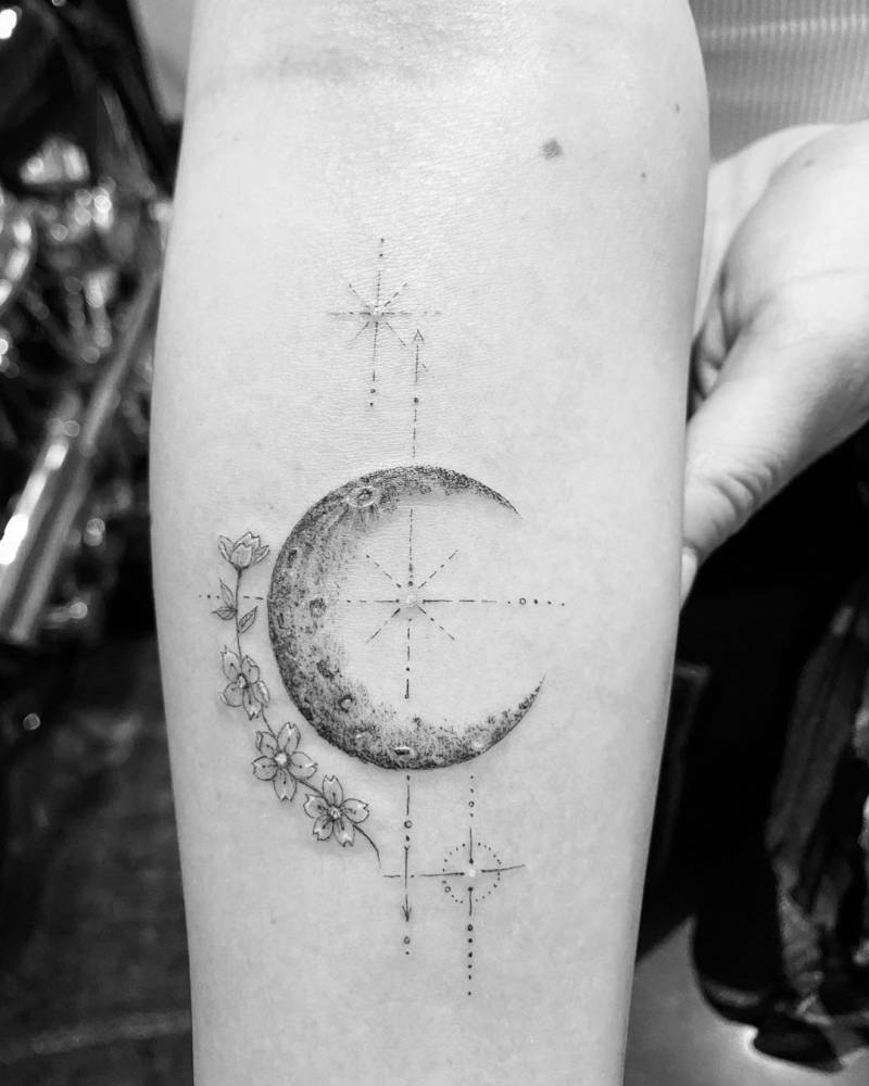 Janel Parrish tattoos: crescent moon with flowers and fine geometric marks on the forearm