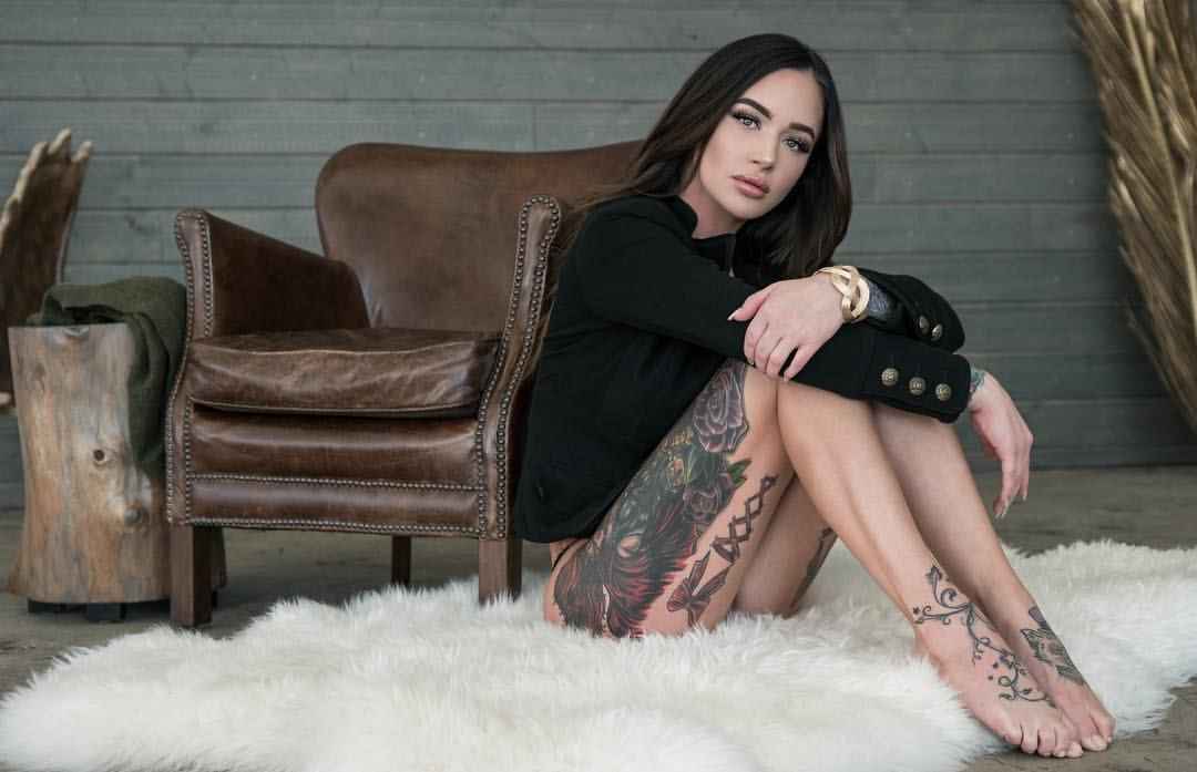 Jessica Wilde tattoos: Large rose, leaves, dark thigh illustration and adjacent angular lines clear; character partly hidden by pose, no invented species or full detail.