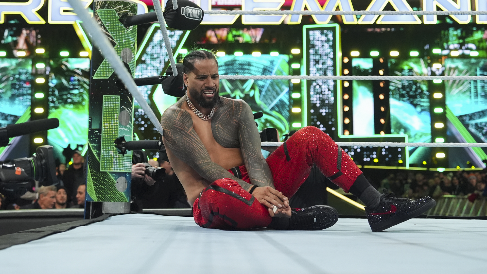 Jimmy Uso tattoos: Both forearms and wrist bands on seated Jimmy in red pants