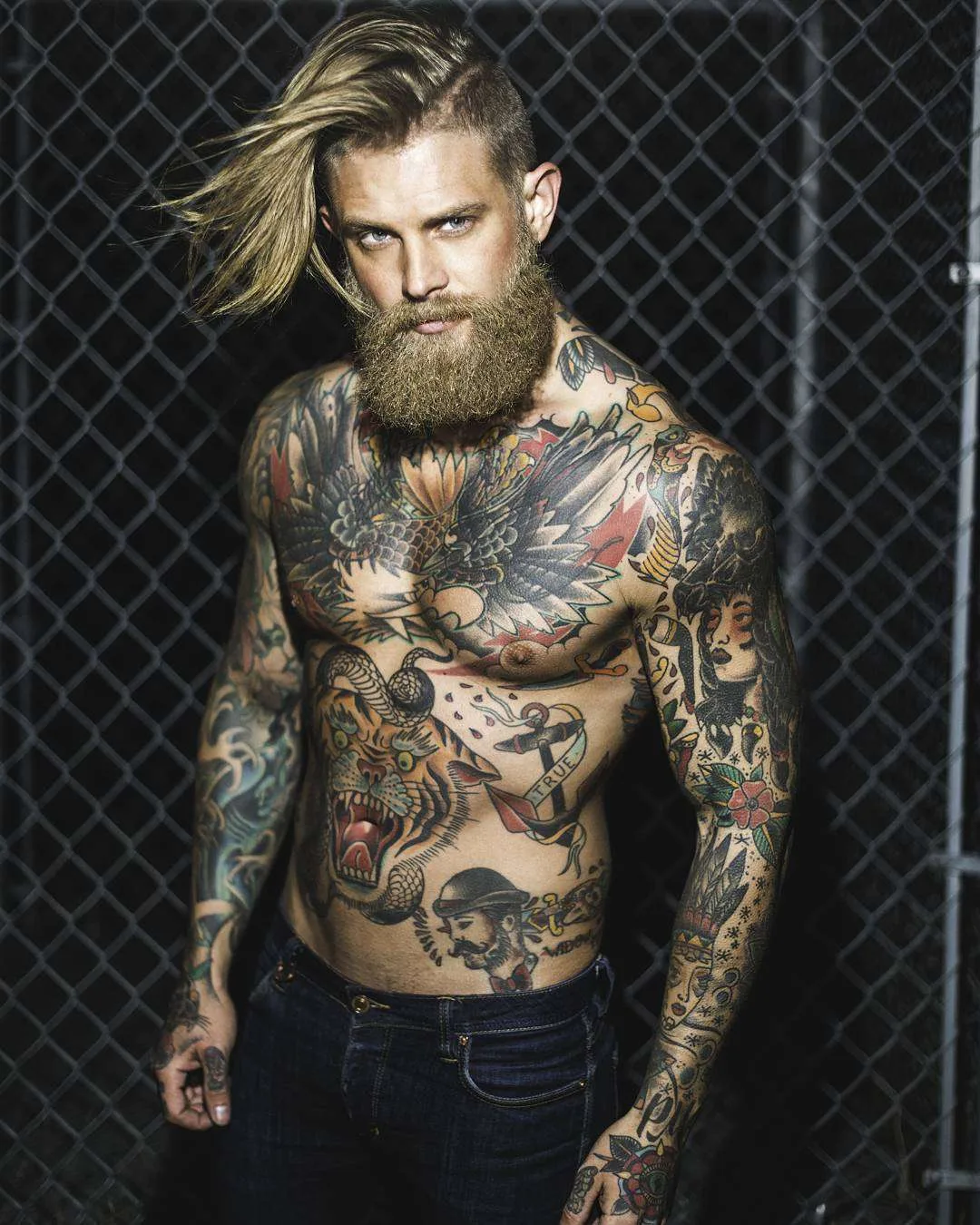 Josh Mario John tattoos: Anchor with a TRUE ribbon and a separate bearded sailor-style portrait on the lower torso.