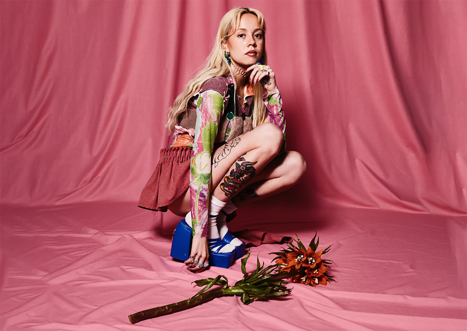 Josie Man tattoos: A separately staged pink-background editorial photograph; distinct colorful leg tattoos and additional arm ink are visible.