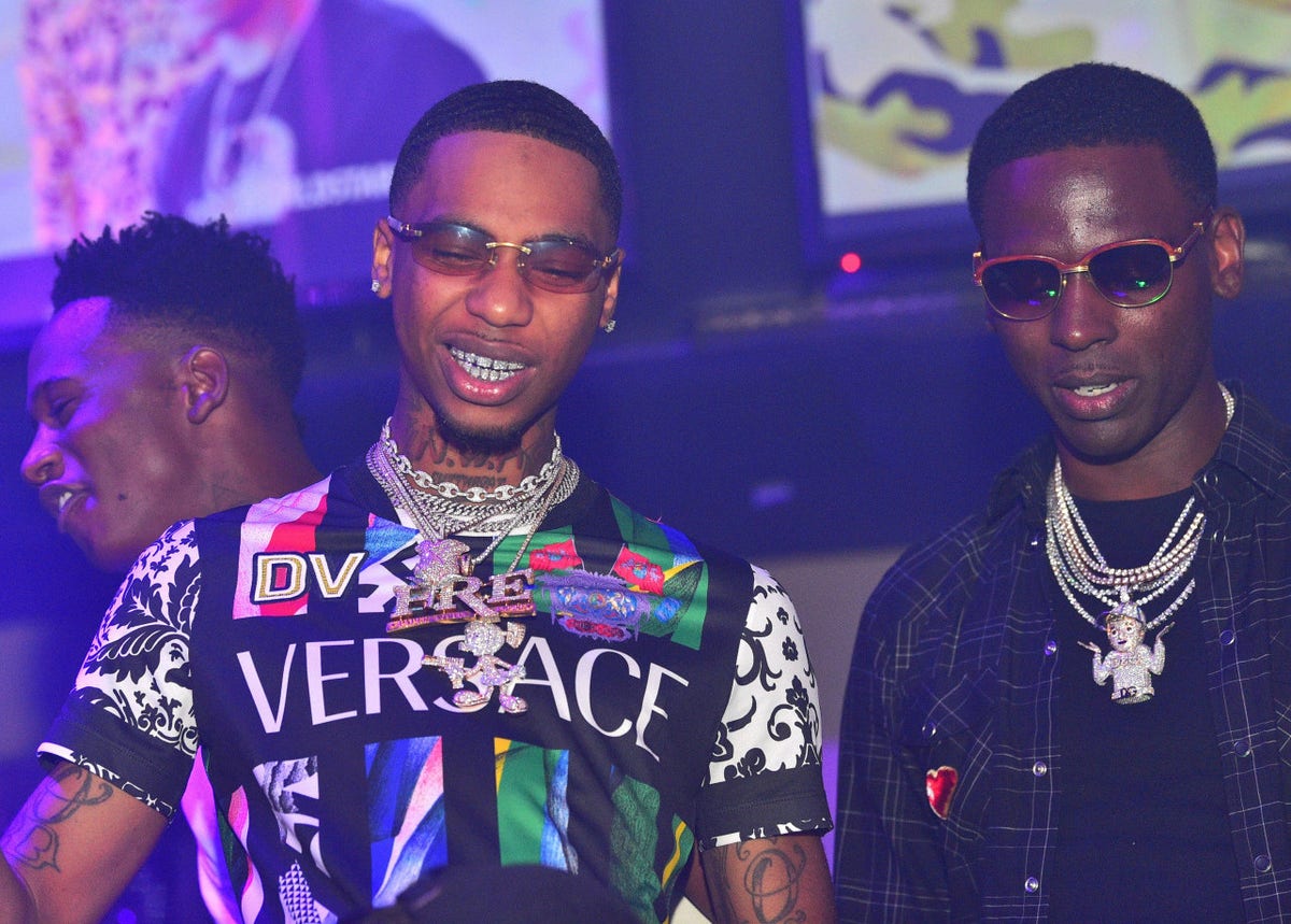 Key Glock tattoos: neck lettering and arm ink in a club portrait