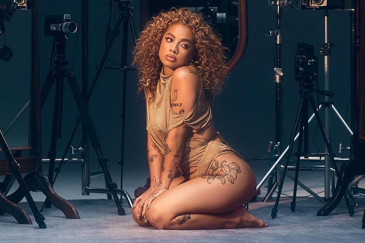 Kiana Ledé tattoos: Gold-outfit studio portrait showing shoulder and thigh placement